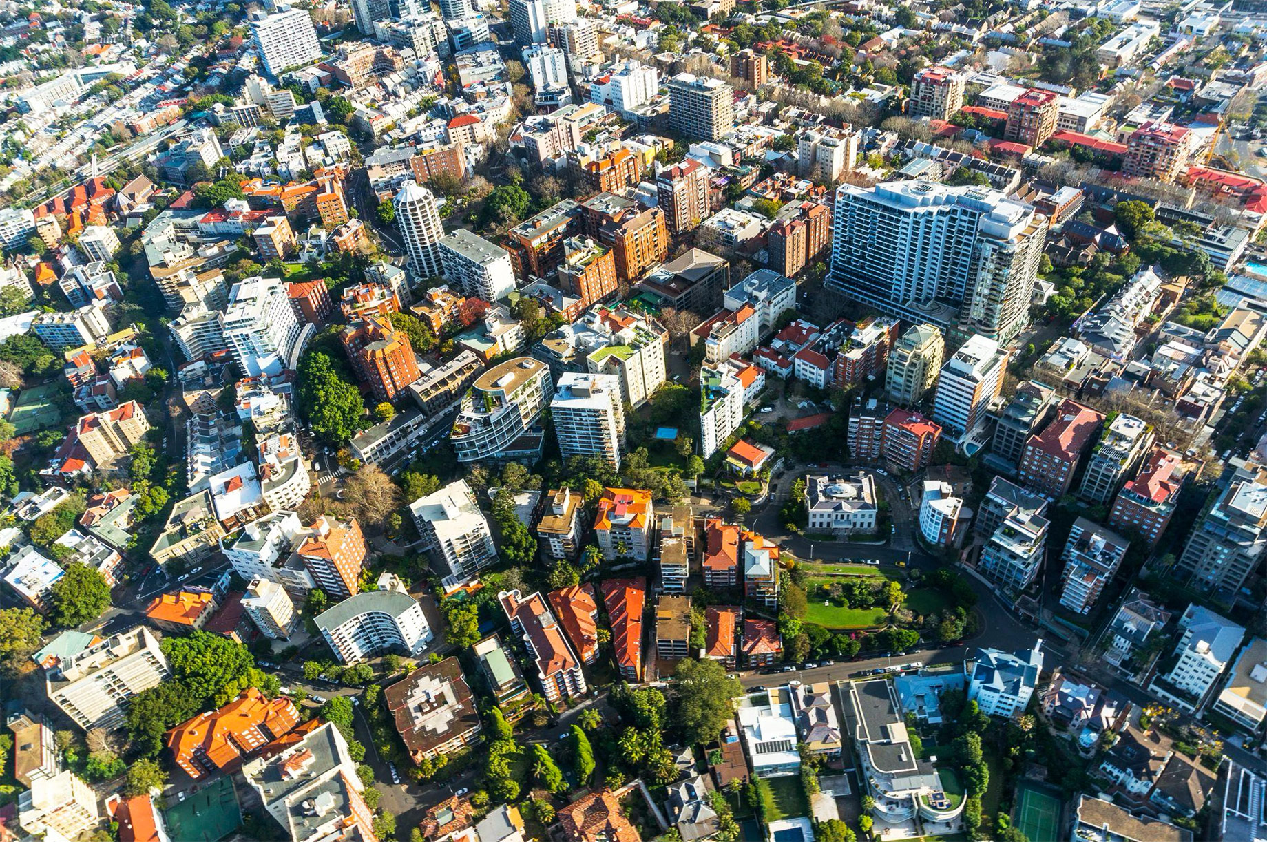 Aerial view of a dense urban residential area with apartment buildings, houses, tree-lined streets, and mixed property types.