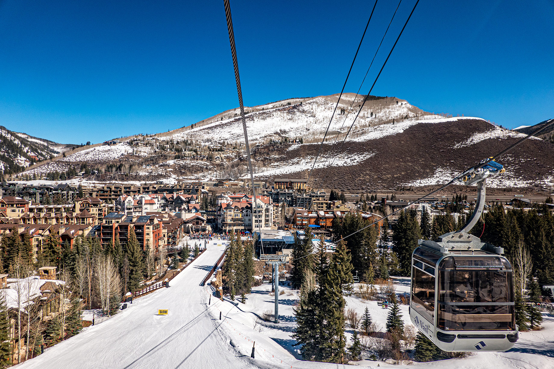 Gondola descending above a snowy ski run and Vail resort village beneath the Colorado mountains.