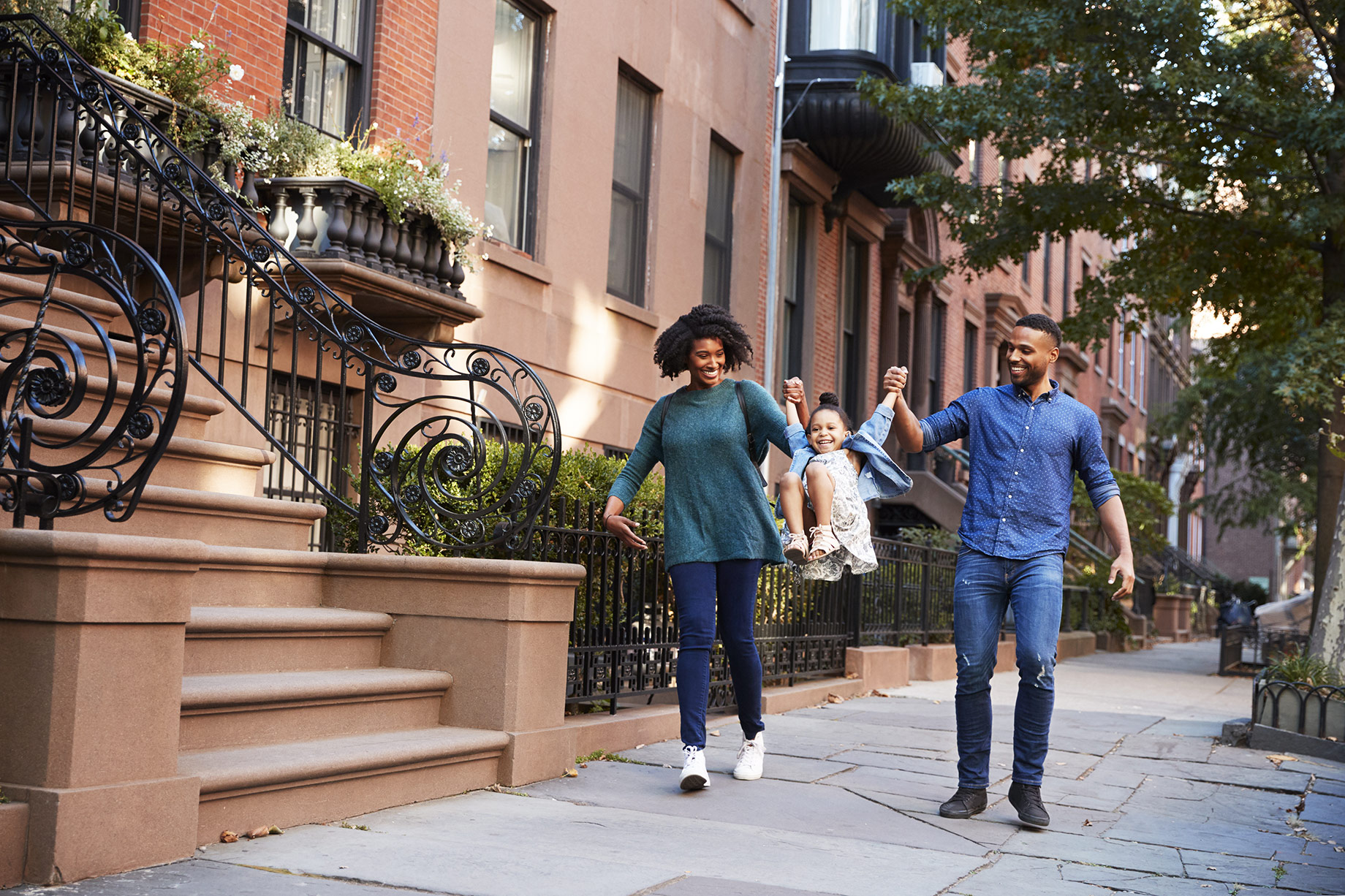 Family walking together along a tree-lined Brooklyn street bordered by historic brownstone homes.