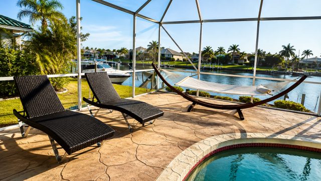 Screened waterfront lanai with swimming pool, lounge chairs, hammock, canal views, boats, and palm trees in Punta Gorda, Florida.