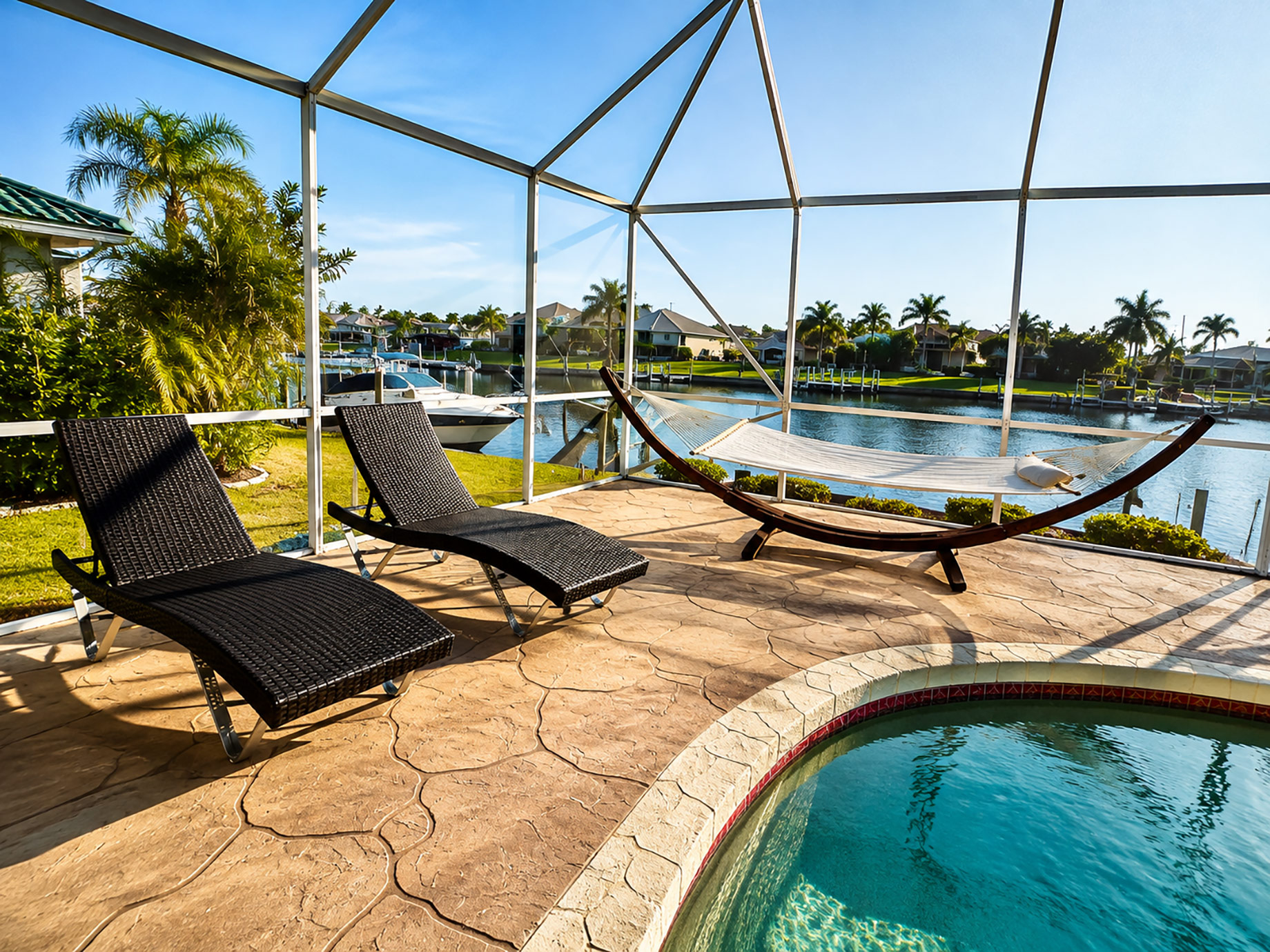 Screened waterfront lanai with swimming pool, lounge chairs, hammock, canal views, boats, and palm trees in Punta Gorda, Florida.