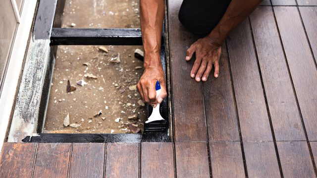 Professional painter applying black anti-rust coating to exposed steel framing beside wooden balcony decking during repair work