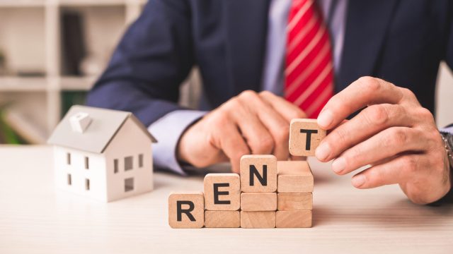 Property professional stacking wooden blocks spelling RENT beside a model house to illustrate data-driven rental pricing.