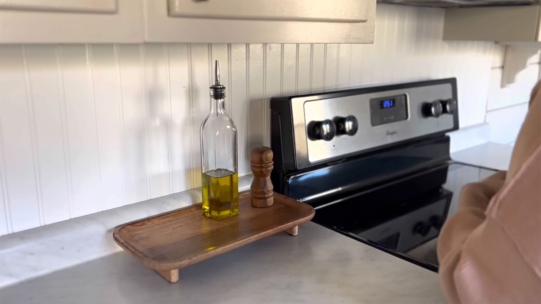 Light-colored kitchen countertop beside a black glass cooktop, with an oil bottle and wooden pepper mill on a raised wooden tray.