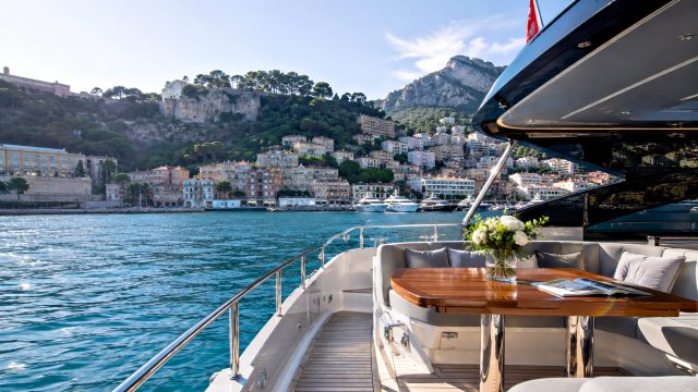 Luxury yacht deck with an outdoor dining area overlooking Monaco’s waterfront, hillside residences, marina, and Mediterranean coastline.