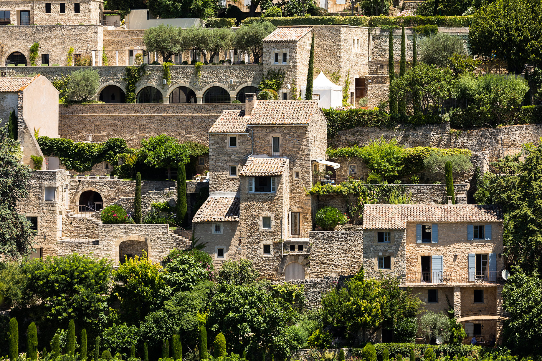 Sunlit stone houses and terracotta roofs in the medieval hilltop town of Gordes, Provence, France.