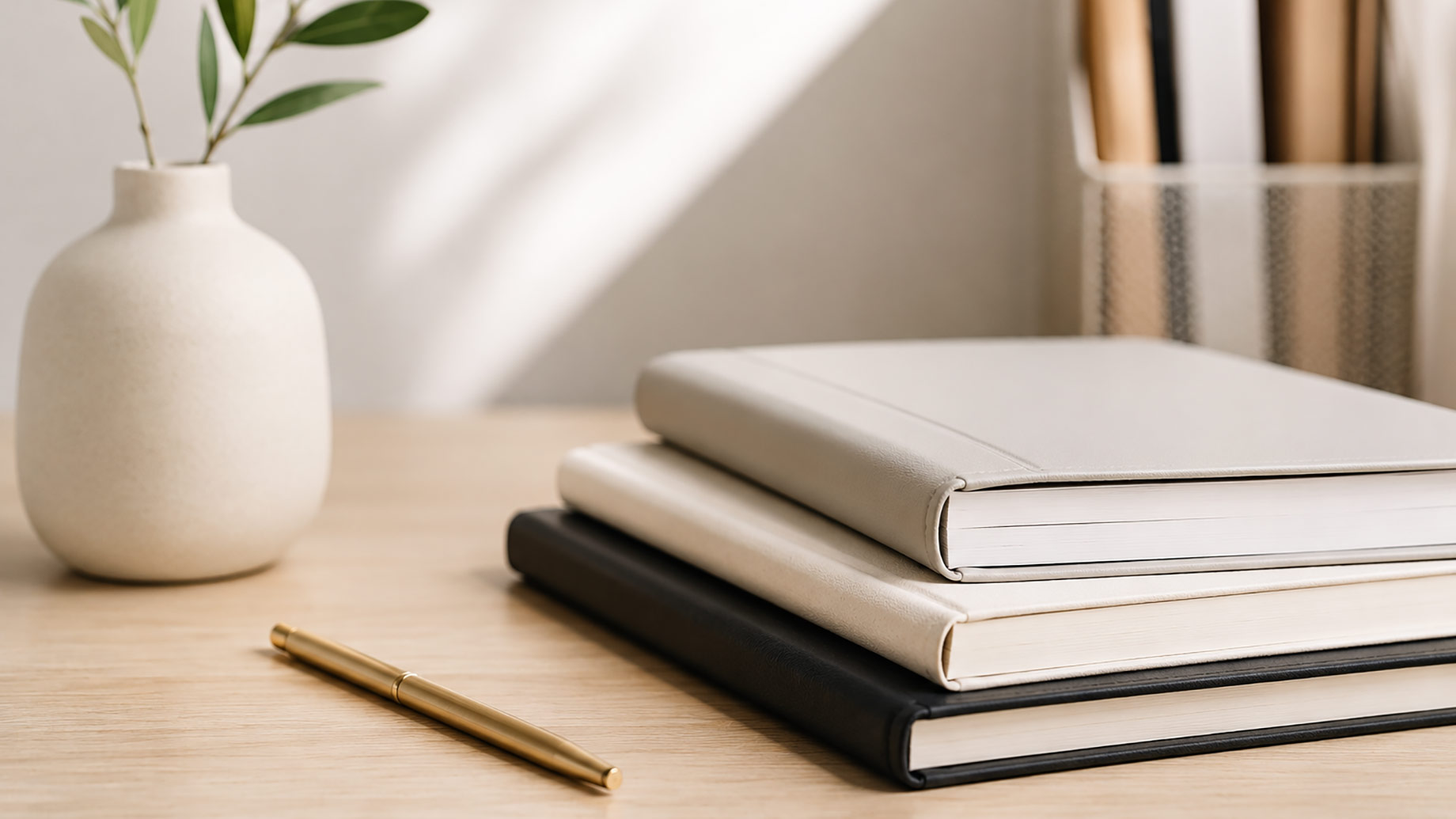Minimalist desk with stacked notebooks, a brass pen, and a leafy plant arranged for MLO licensing study, planning, and document organization.