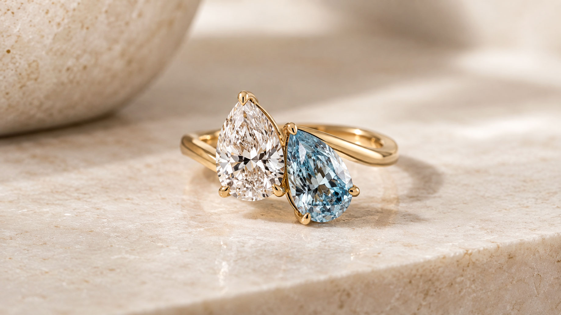 Gold Toi et Moi ring featuring two pear-cut stones, one clear and one pale blue, set side by side on a polished band.