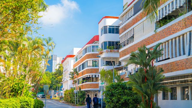 White heritage buildings with red-brick bands and striped awnings line a leafy street in Singapore’s Tiong Bahru neighbourhood.