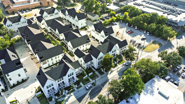 Aerial view of white townhomes with dark roofs, tree-lined streets, surface parking, and a rooftop garage in Arlington, Texas.