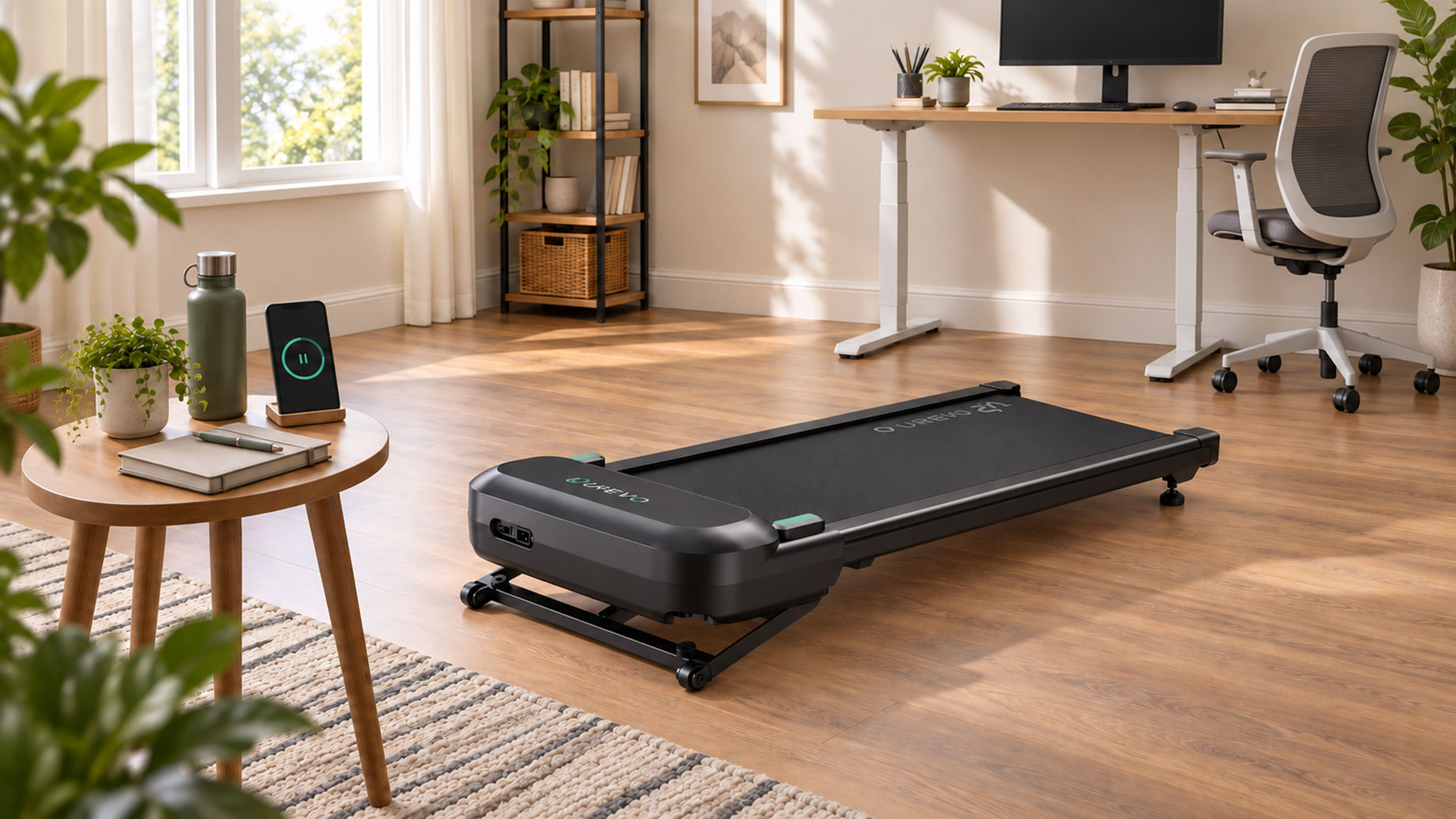 Walking pad on a wooden floor in front of a standing desk, with a phone displaying a pause symbol on a nearby side table.