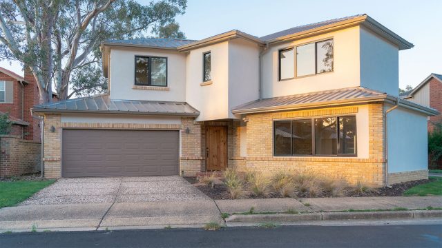 Two-storey home with pale brickwork, white render, a double garage and a eucalyptus tree in warm afternoon light.