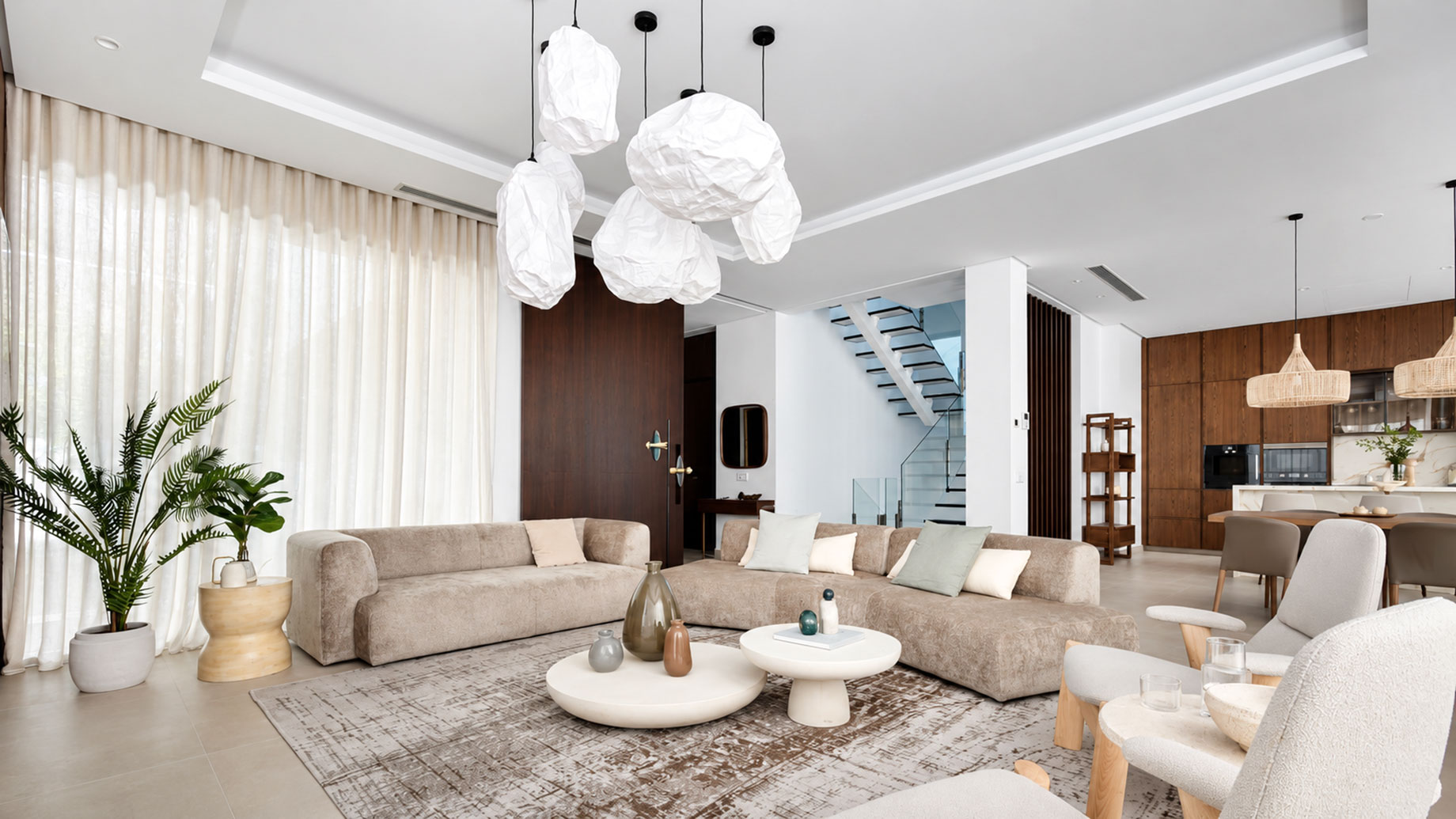 Marbella villa living room with taupe sofas, sculptural white pendant lights, round coffee tables and wood kitchen cabinetry.
