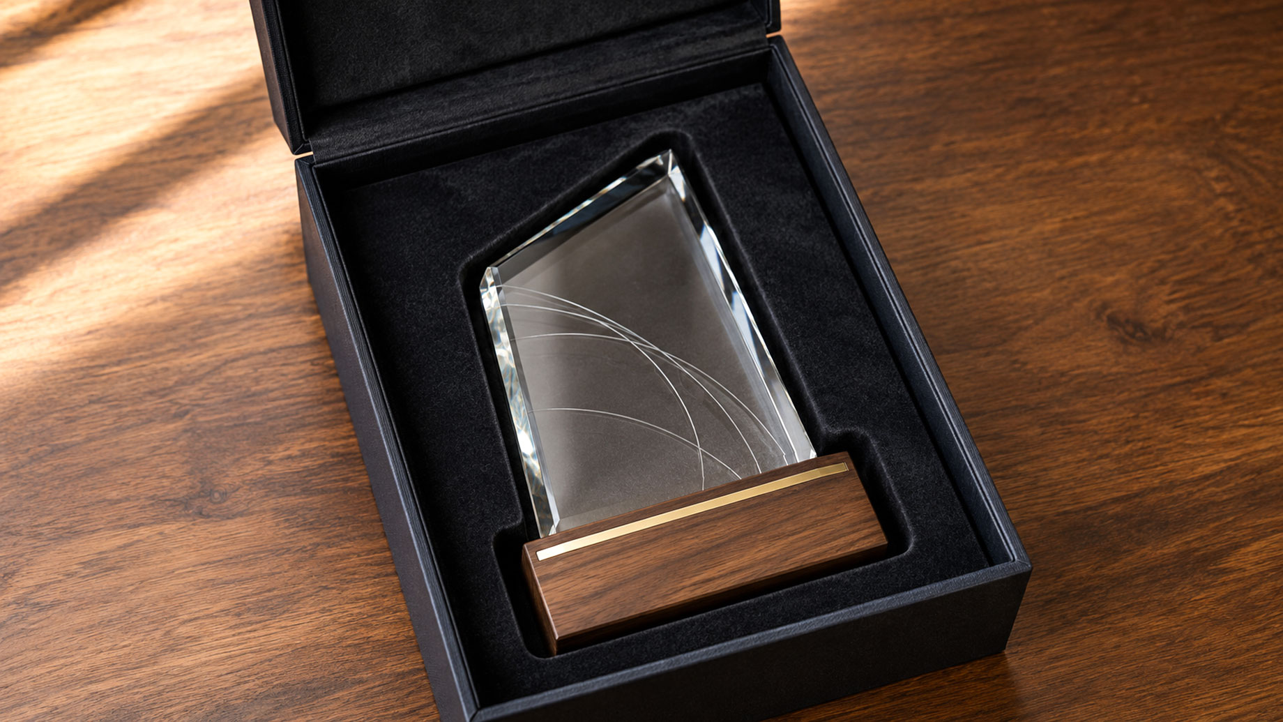Clear award with a wooden base resting inside a fitted black presentation case on a wooden table.