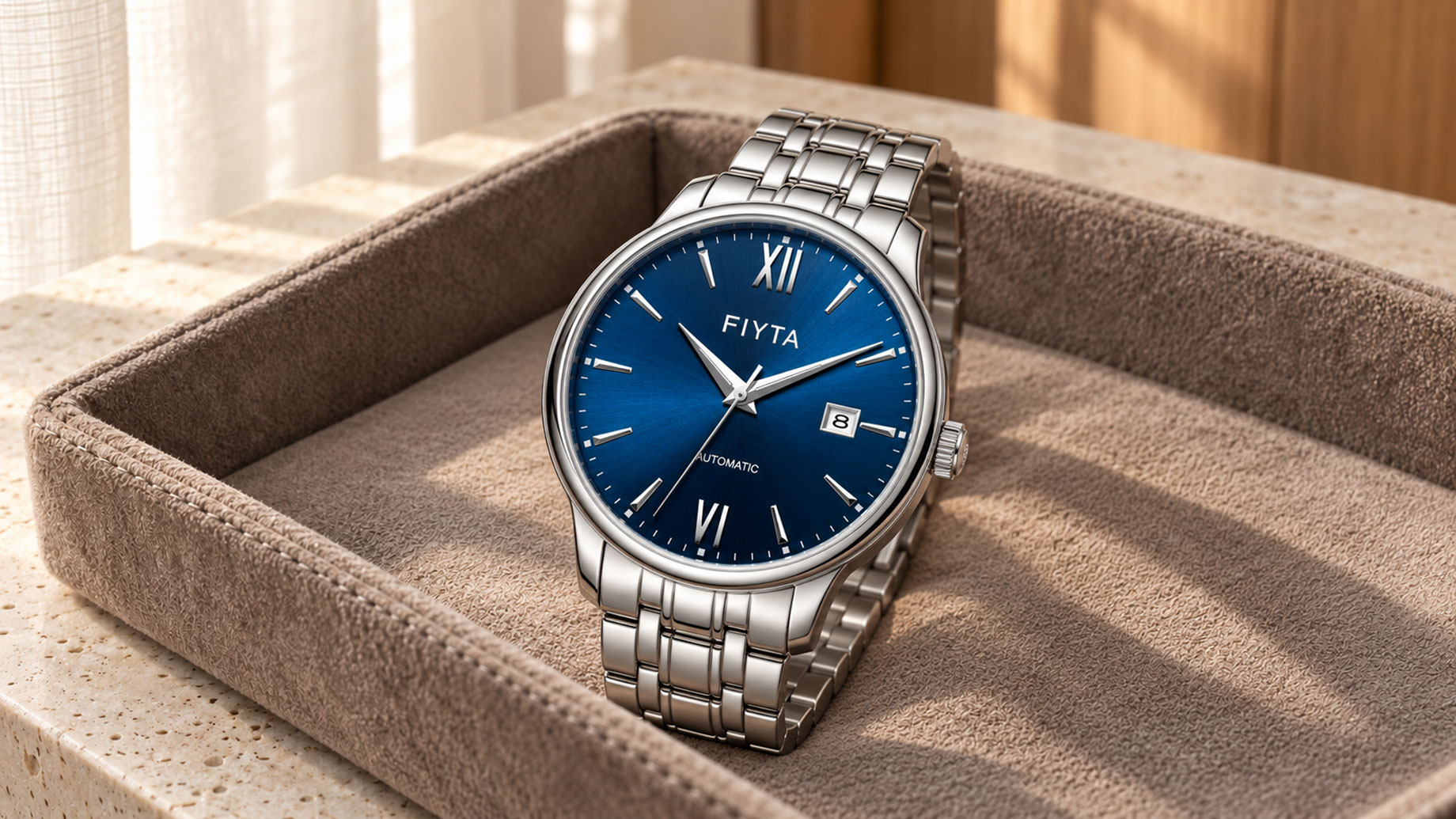 Blue-dial FIYTA watch with a stainless steel bracelet resting in a suede valet tray on a sunlit stone console.