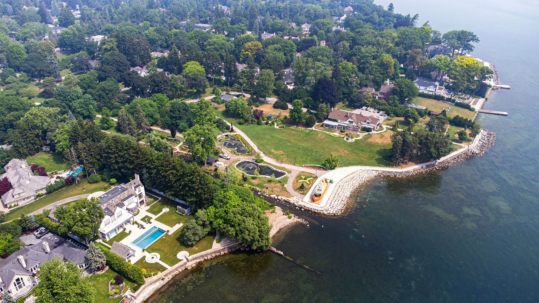 Aerial view of Gairloch Gardens in Oakville, showing lawns, ponds, winding paths, mature trees, and neighbouring homes beside Lake Ontario.