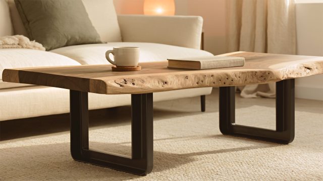 Live-edge wood coffee table with black metal legs, a ceramic mug, and a closed book, set on a cream rug in front of a sofa.