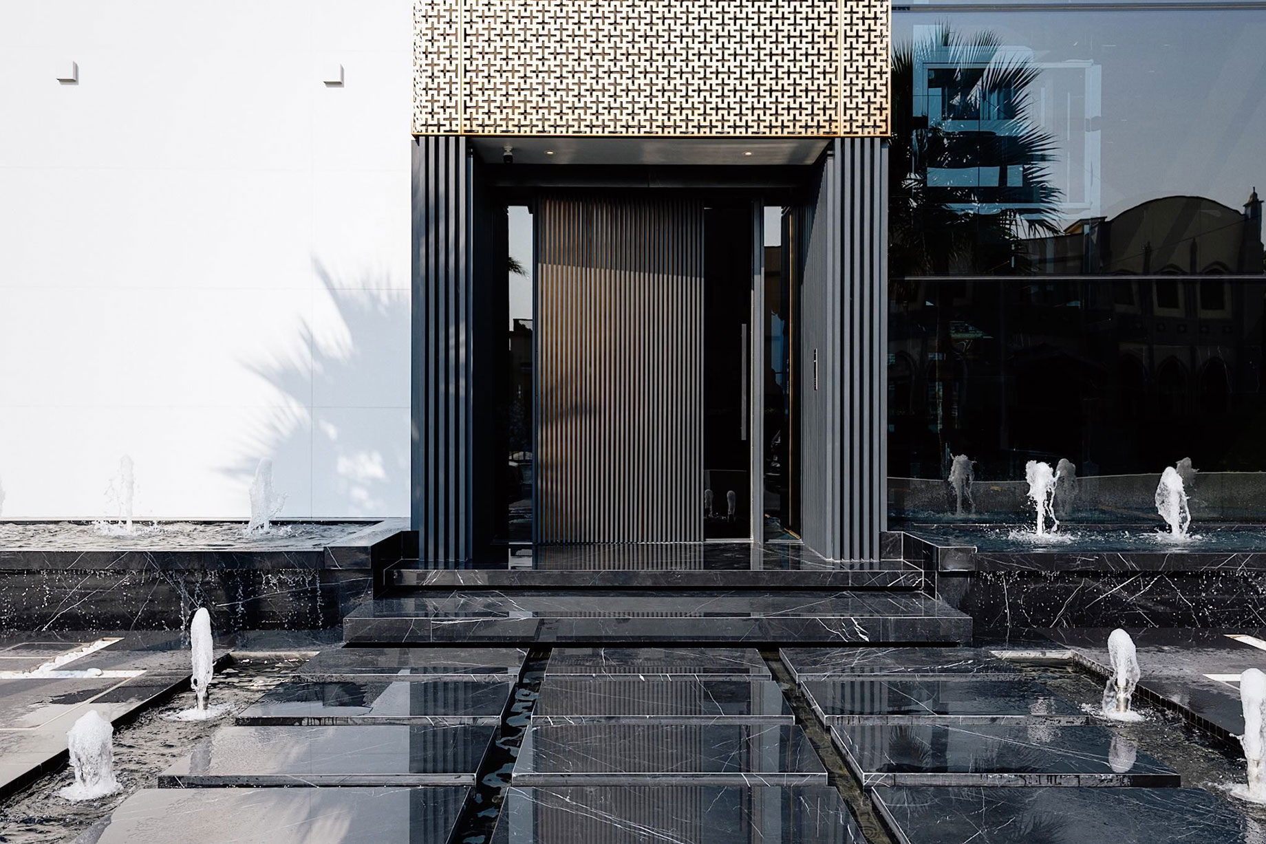 Entrance of a luxury Palm Jumeirah villa with a black stone water feature and fountains.