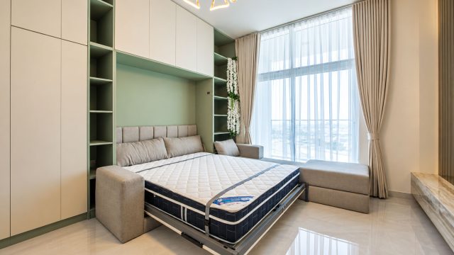 Open Murphy bed with a white mattress, beige sofa seating and sage-green shelving beside a tall curtained window.