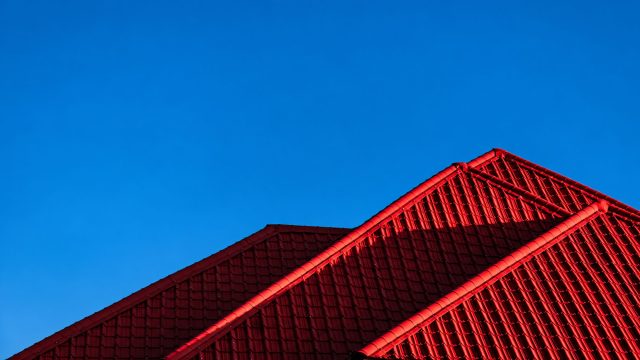 Intersecting red tiled roof slopes with curved ridge caps and strong shadows beneath a clear blue sky.