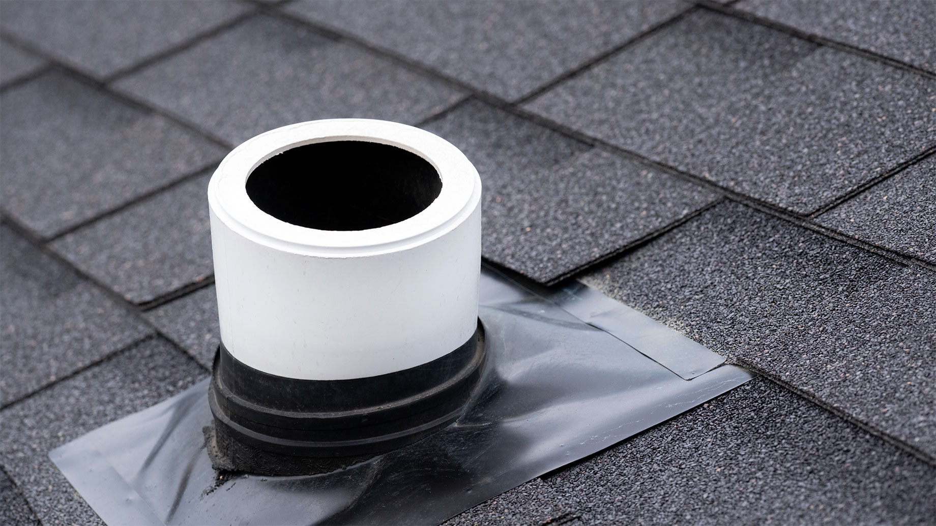 Open white plumbing vent pipe with a black rubber boot and flashing on a gray asphalt-shingle roof.