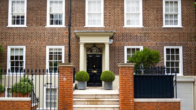 Brick house in West London with white sash windows, a black front door, cream entrance columns, stone steps, and iron railings.
