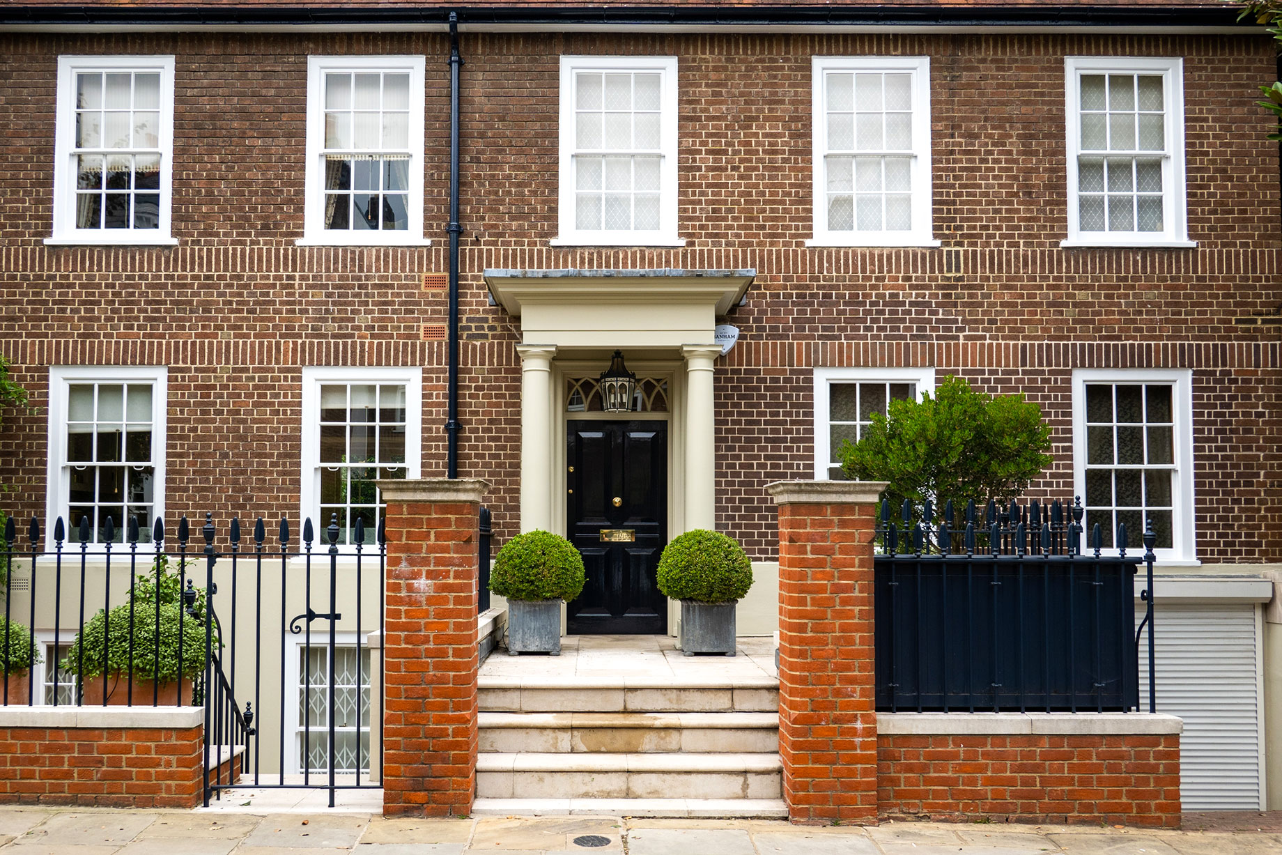 Brick house in West London with white sash windows, a black front door, cream entrance columns, stone steps, and iron railings.