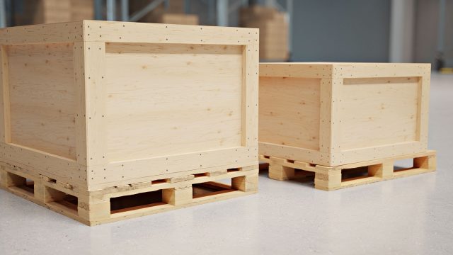 Two plywood shipping crates with timber framing and wooden pallet bases on a concrete warehouse floor.